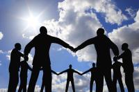 silhouettes of people holding hands to form a circle against a blue sky with white puffy clouds